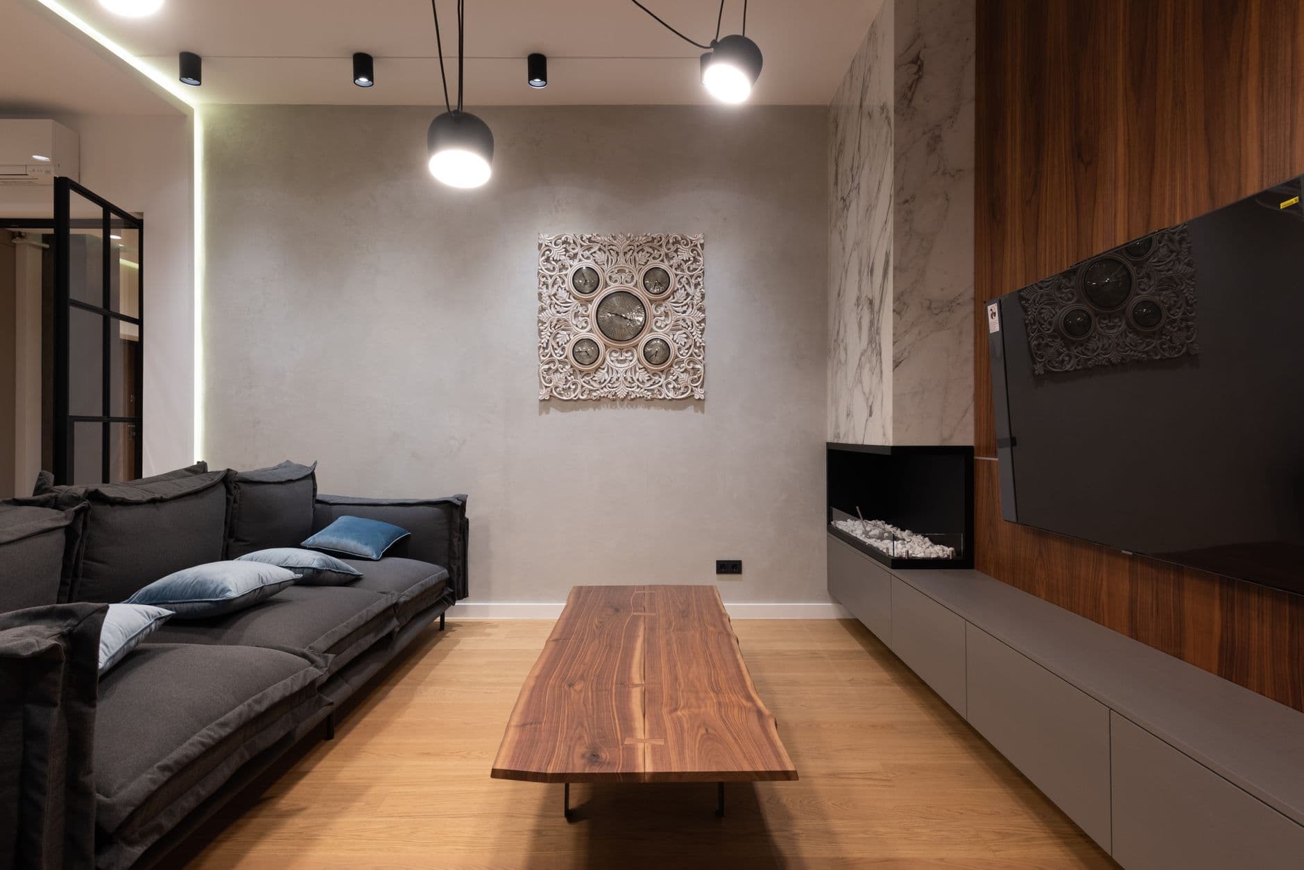 A spacious living room with a cushioned sofa, a wooden coffee table and a television mounted on a wooden wall beside a fireplace