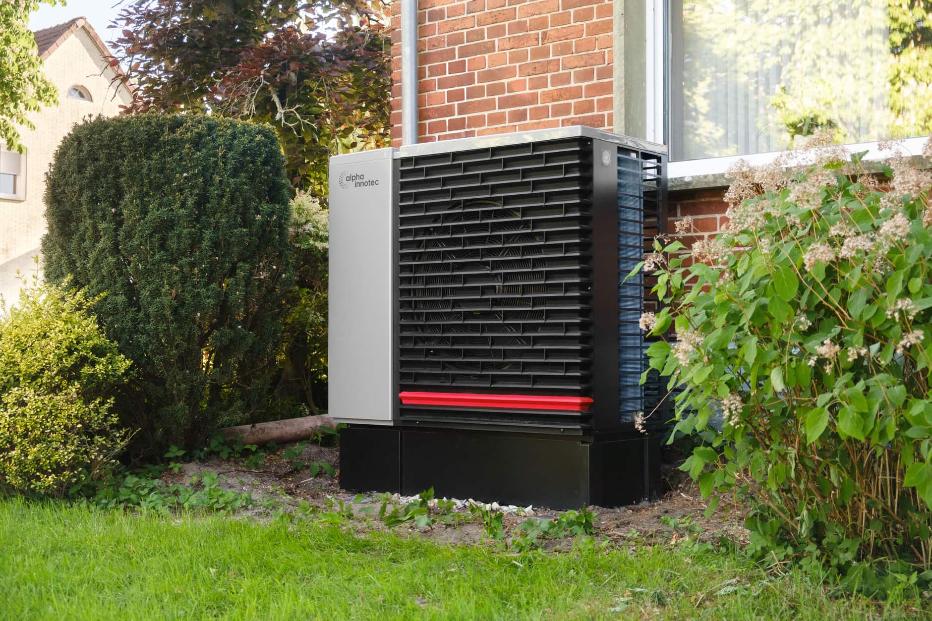 An air-source heat pump unit standing in a garden beside a brick house