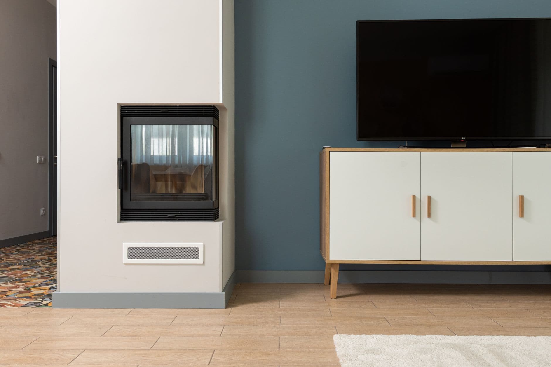 A contemporary apartment with a television on a white stand beside a fireplace set into the wall
