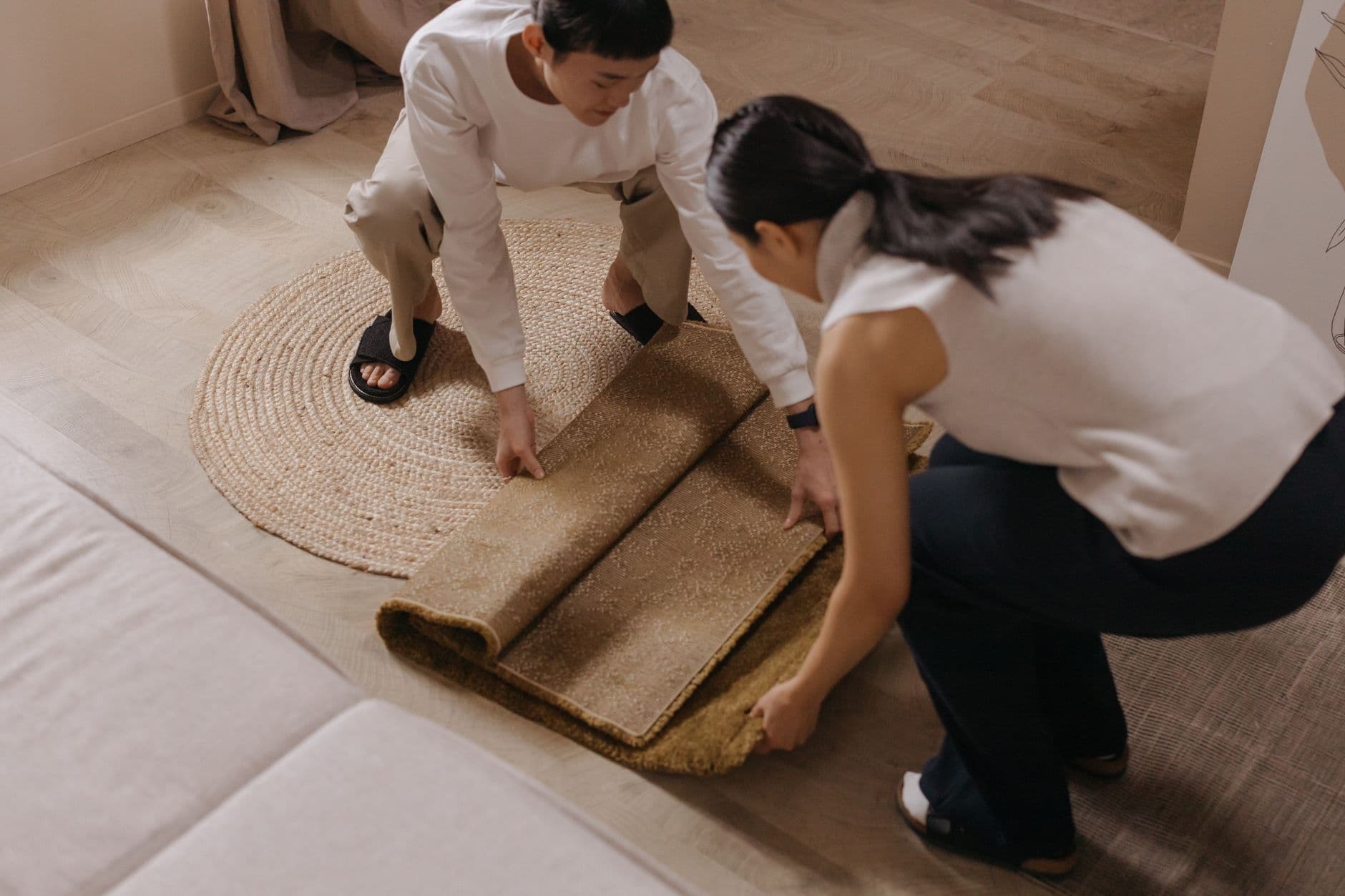 Two people unrolling a large rug across the floor of a furnished living room