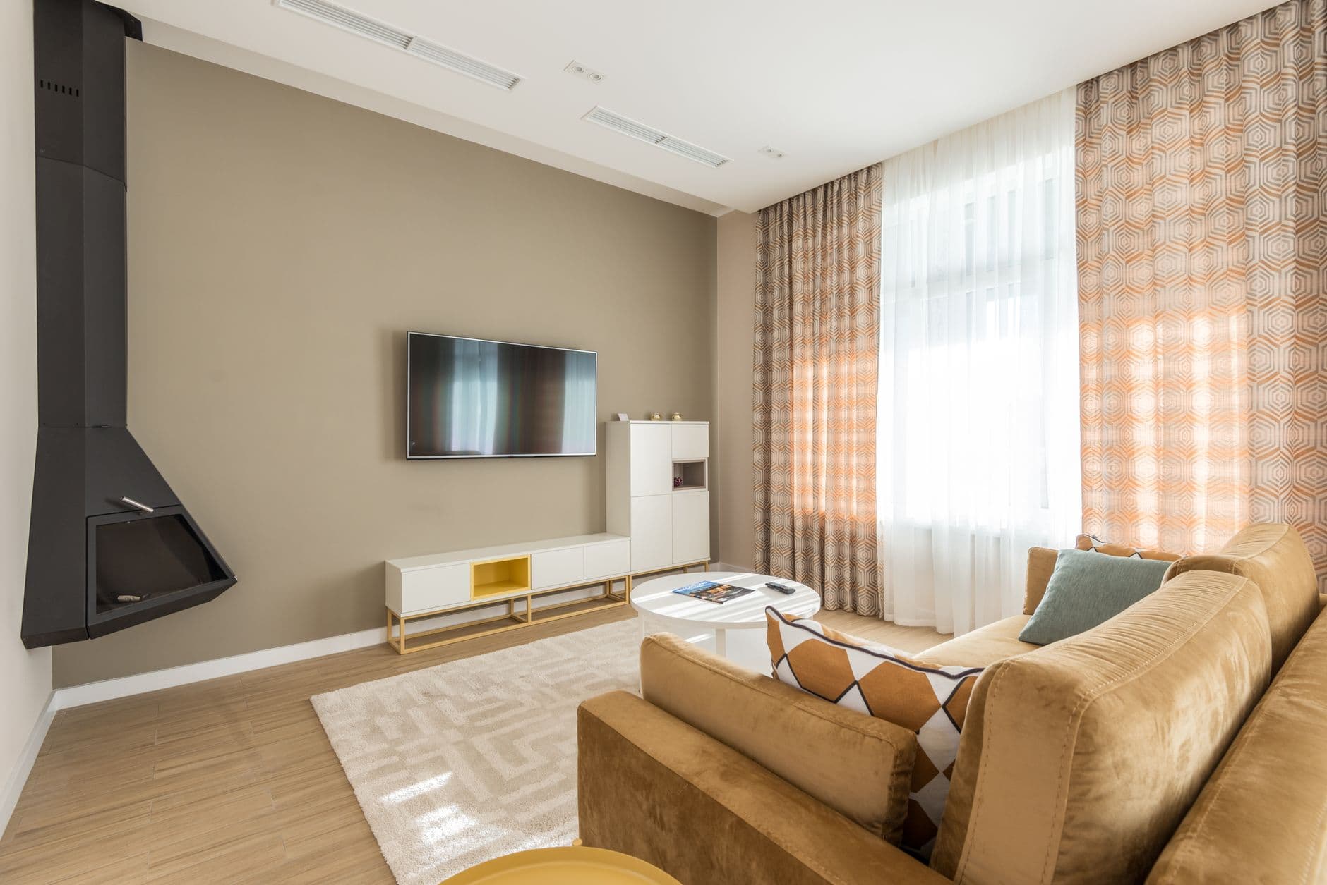 A living room with a beige sofa and a flat-screen television mounted on the wall above a low console