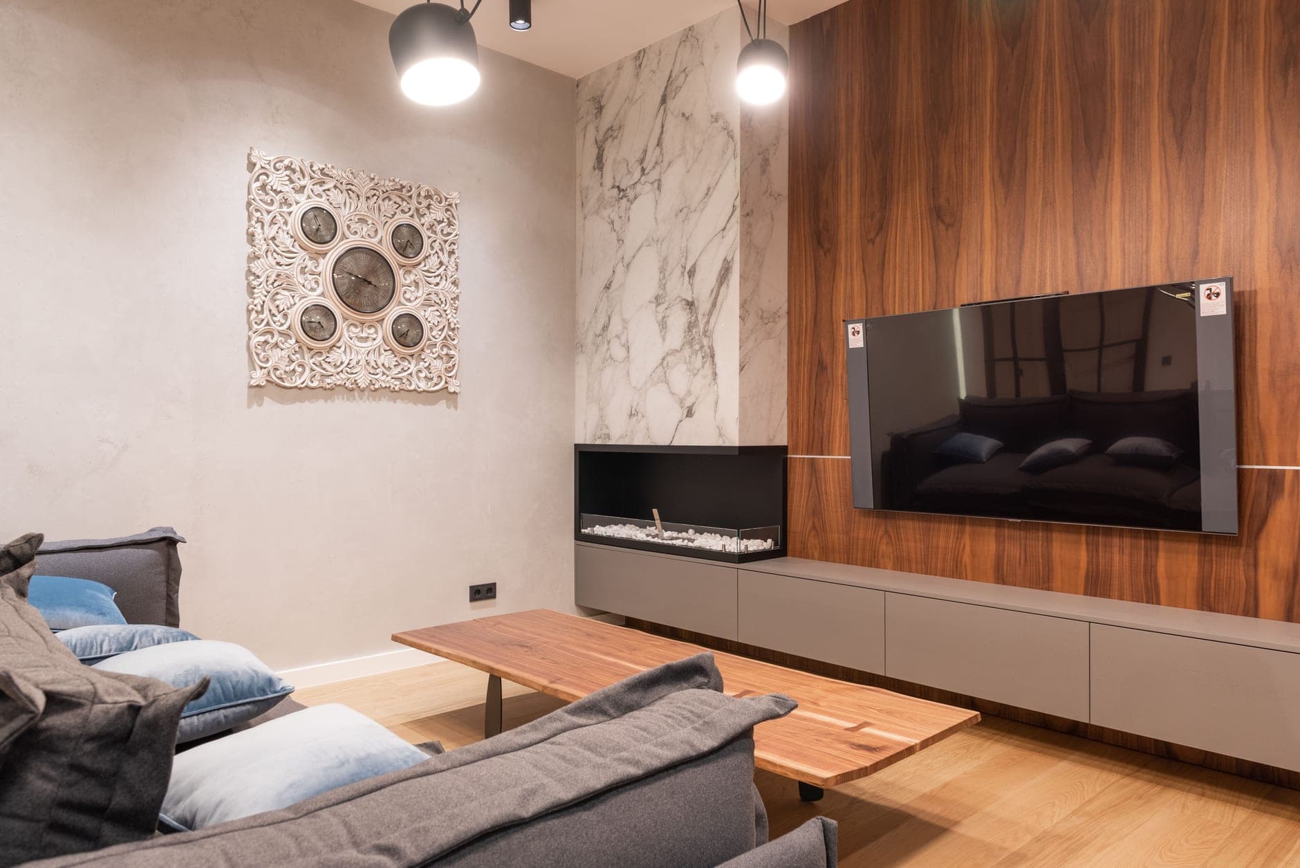A linear fireplace recessed into a marble wall beside a wall-mounted television in a modern apartment