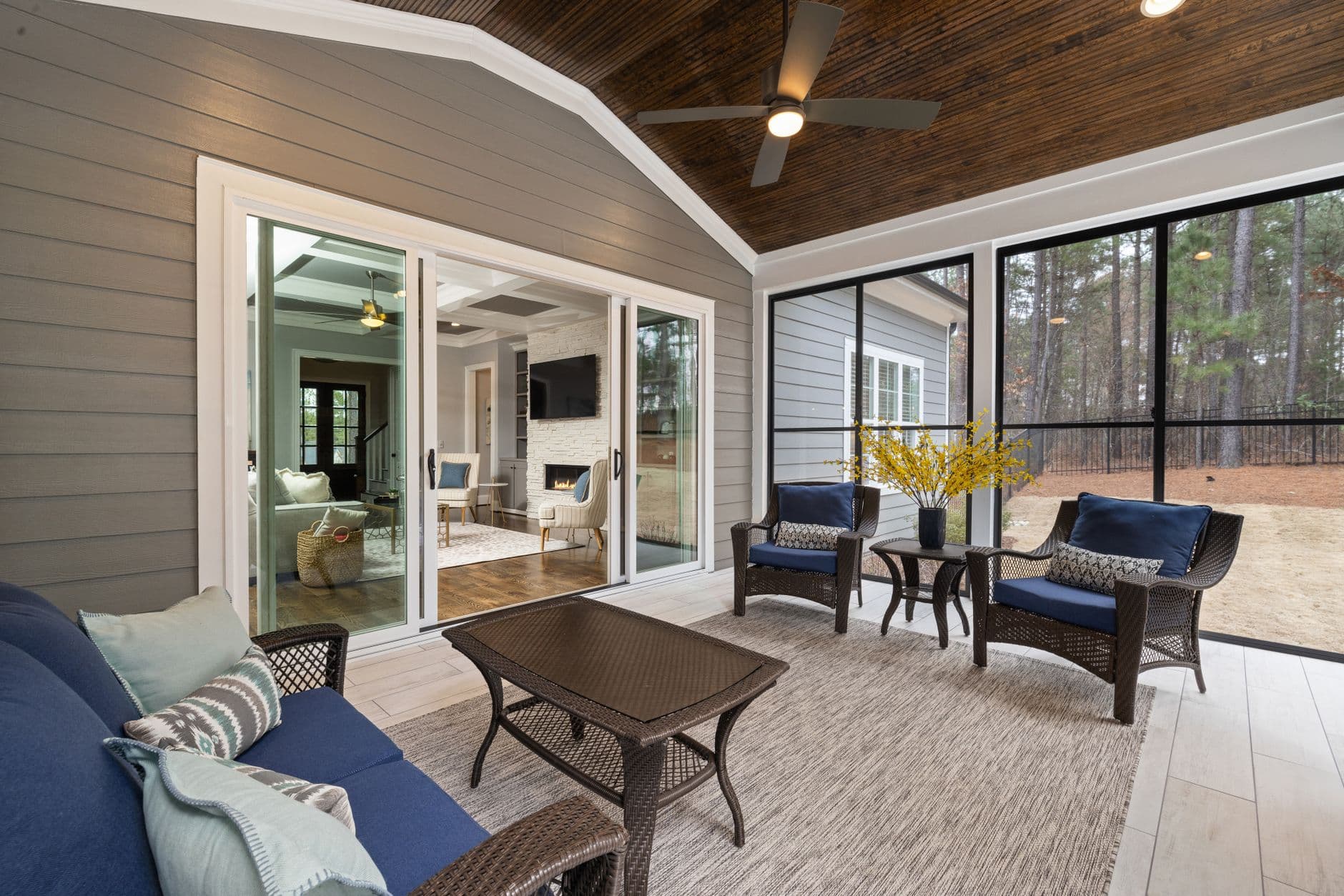 A sunlit enclosed porch furnished with wicker chairs, looking out onto greenery