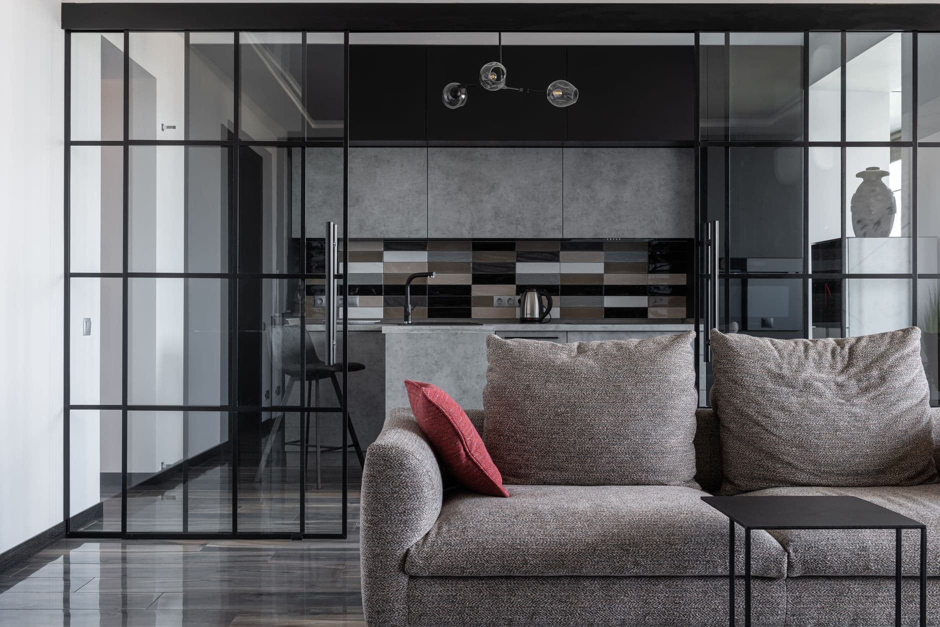 A glazed partition wall dividing a living room from a kitchen, seen from the sofa