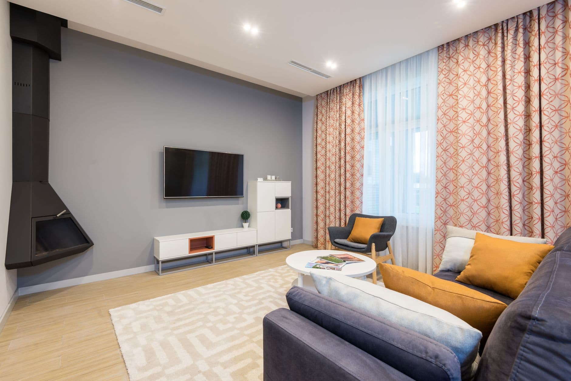 A spacious living room with a couch facing a wall-mounted television beside a white cupboard and a fireplace